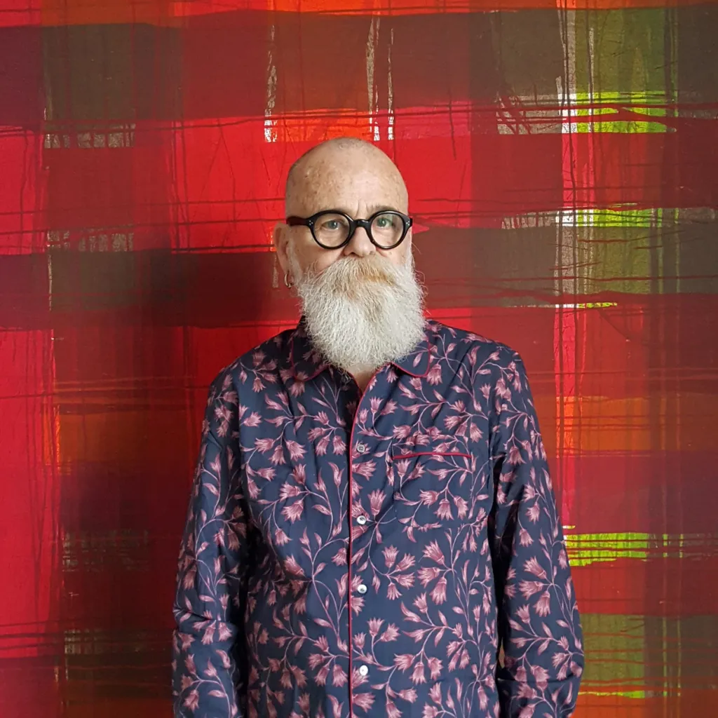 Photograph portrait of artist AA Bronson against a red and green check backdrop
