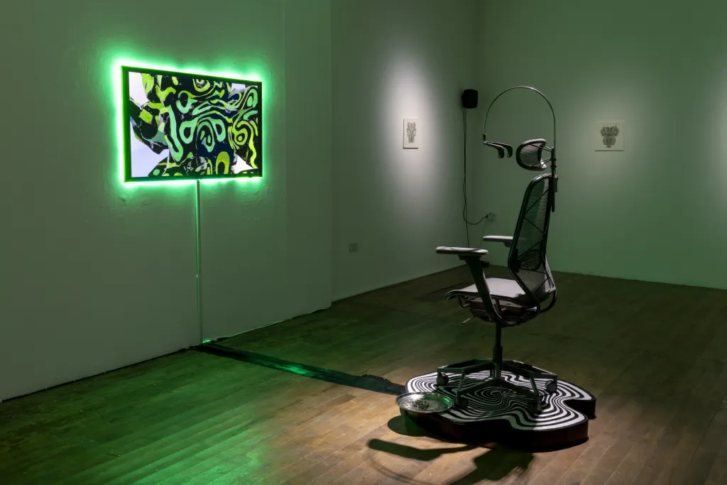 White wall gallery with a wooden floor and green lighting, a gamer chair sits on a platform facing a TV screen depicting a green design.