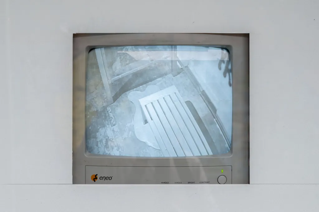 An old grey TV monitor with CCTV footage of the inside of a bus shelter, with white framing the TV.