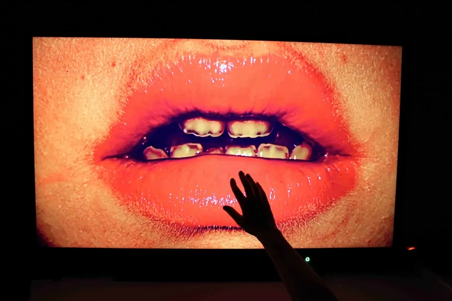 image of a close up of a mouth with blackened teeth on a black background, a hand is reaching up to the bottom lip 