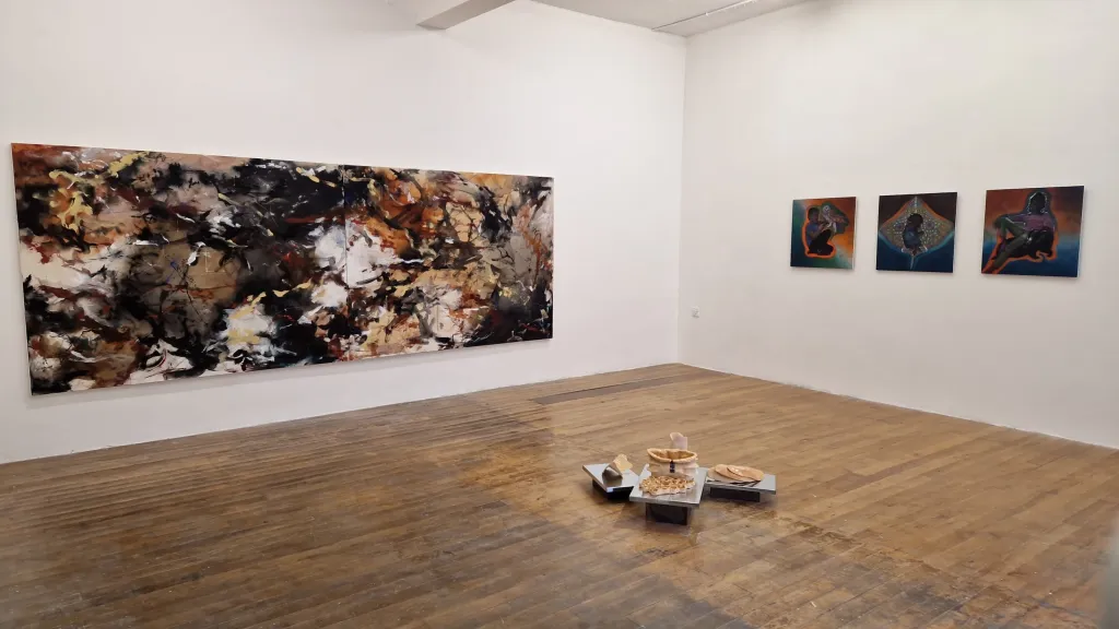 Exhibition documentation in a white wall gallery with wooden floors, one large painting hangs on the left wall and three smaller paintings hang on the right wall, a small sculptural assembledge sits in the middle of the floor. 