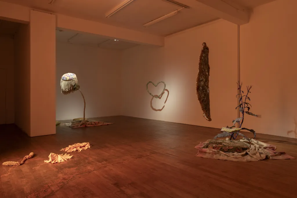 White wall gallery with a wooden floor and dusty orange lighting, installation view with abstract sculptures.