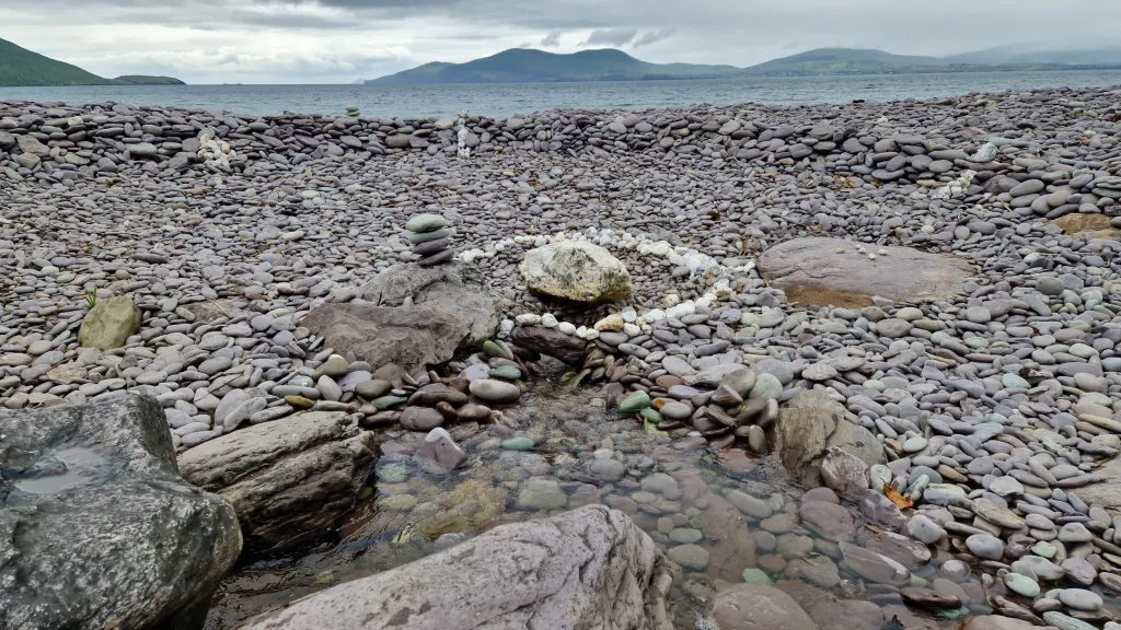 Stoney beach facing the sea, a circle of white stones surrounding a large stone behind a small rock pool. 