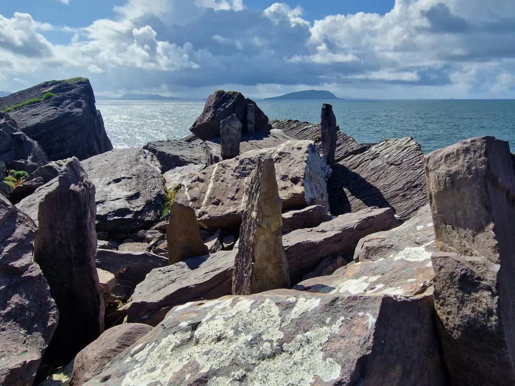 Large rocks in front of the sea, severeal slabs of rock stand verticly amongst the horizontal rocks. 